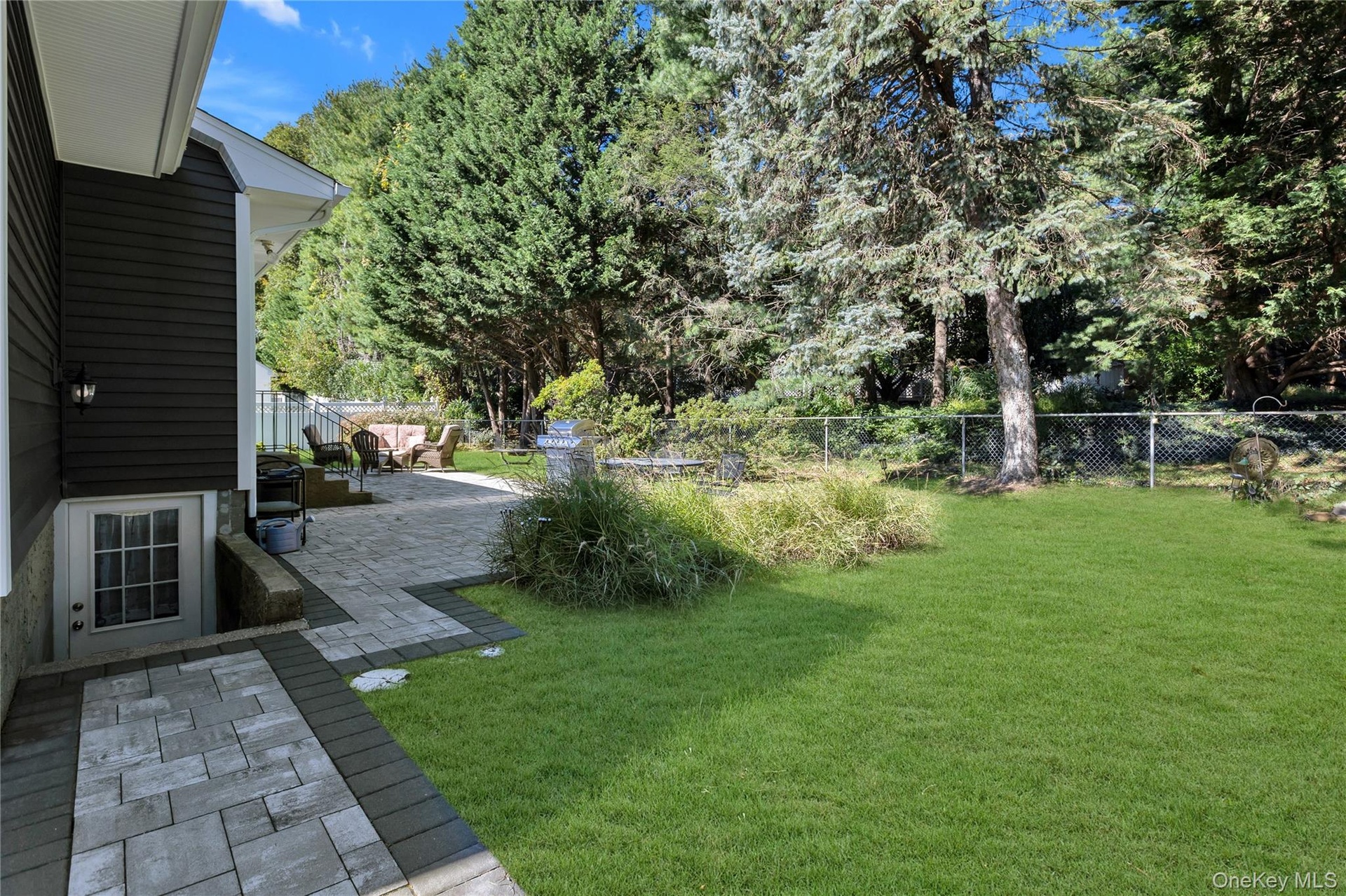 Expansive yard featuring a manicured lawn, mature trees, and a spacious paver patio