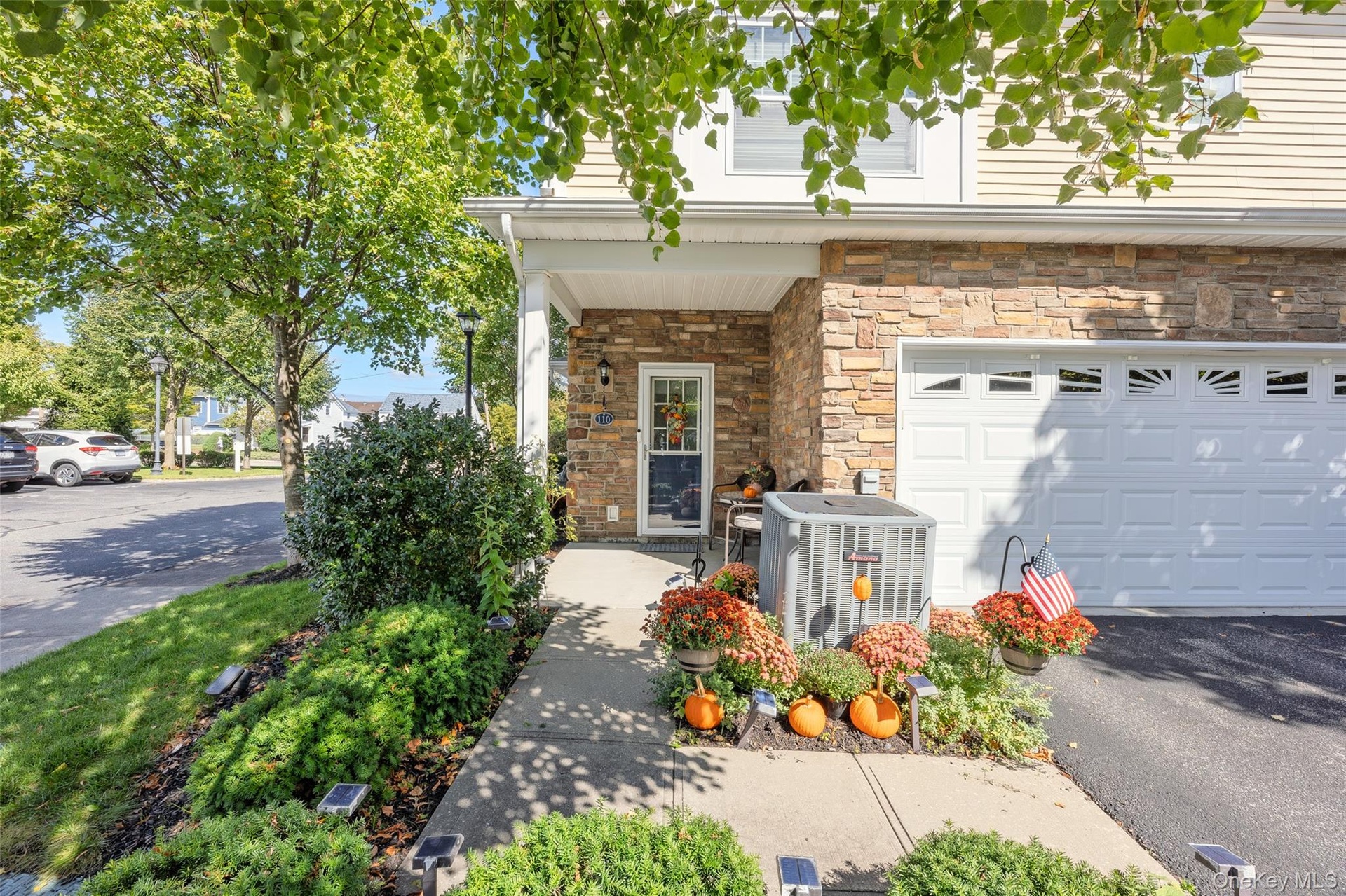 Stone veneer facade with a two-car garage, covered porch entry, and mature landscaping
