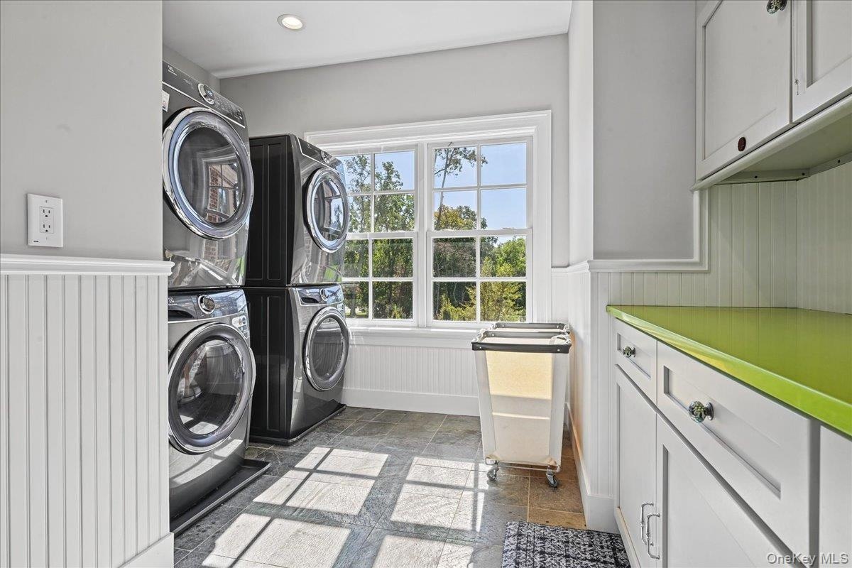 Tile flooring, window with exterior scenery, beadboard wainscoting, white cabinetry, and a bright green countertop