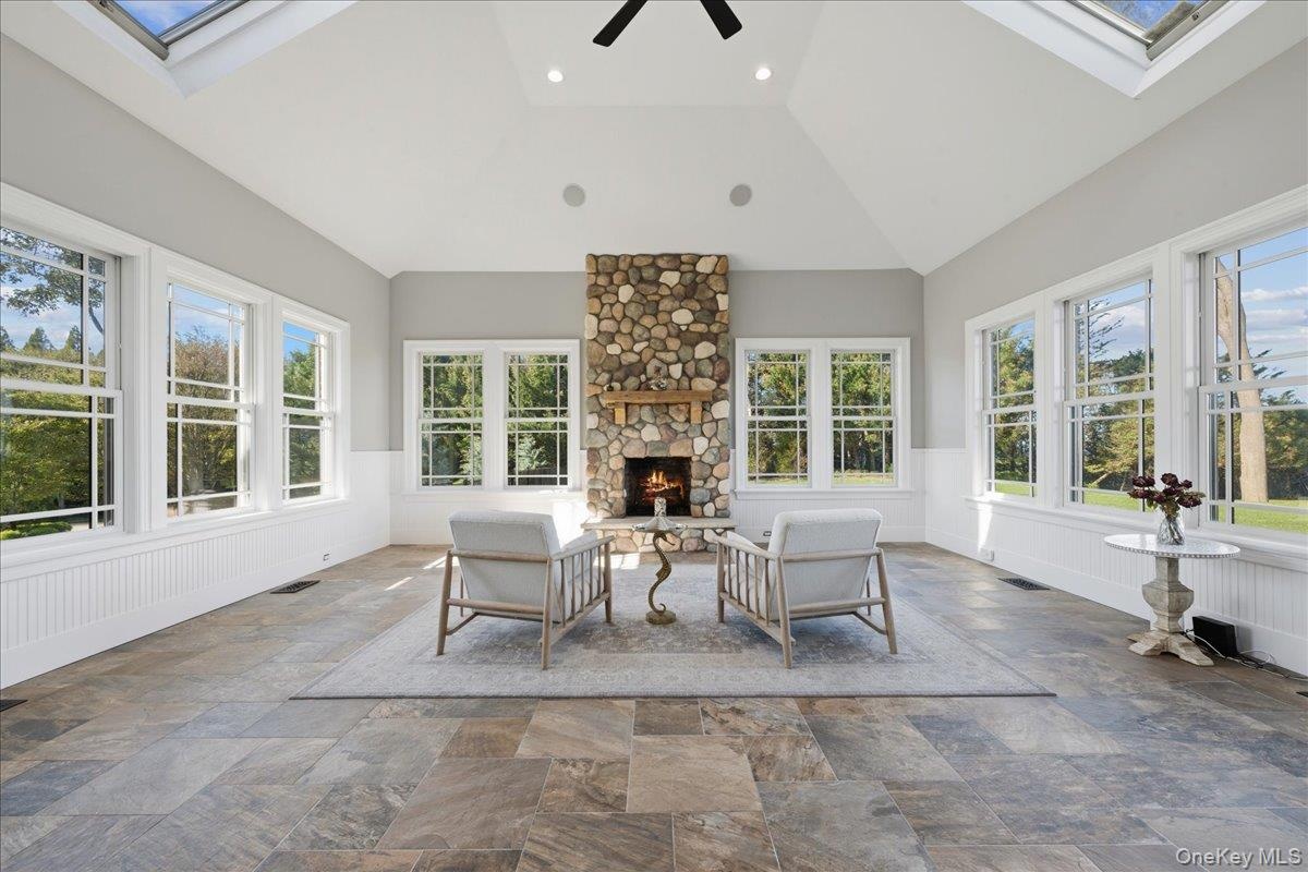 Vaulted ceiling with skylights, stone fireplace with wood mantel, tile flooring, and multiple windows with white trim