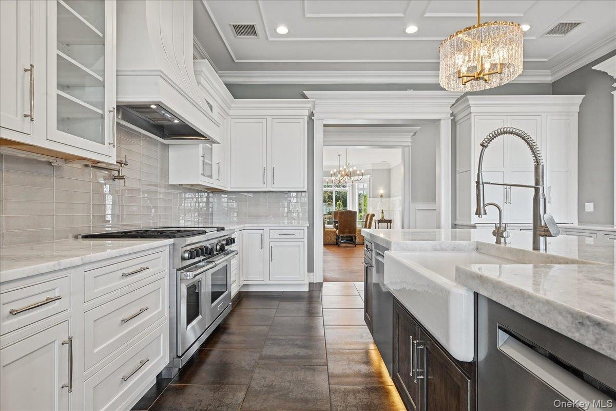 White cabinetry with glass-front uppers, stainless steel range, light-toned subway tile backsplash, and a farmhouse sink with a gooseneck faucet