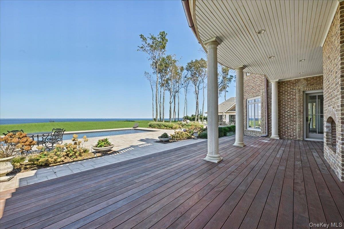 Expansive outdoor deck with dark wood-finish flooring, brick exterior, and white columns