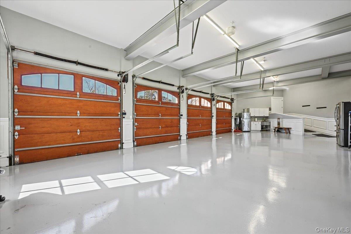 Multiple wood-finish garage doors with arched window panels, expansive light gray flooring, exposed overhead support beams, recessed lighting, and wal