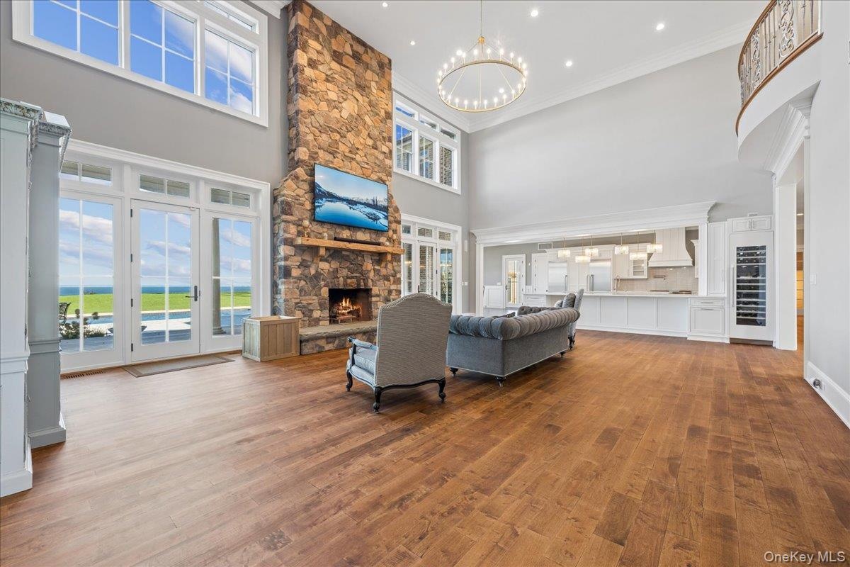 Two-story stone fireplace, wood-finish flooring, white double doors, upper transom windows, and a built-in wine refrigerator