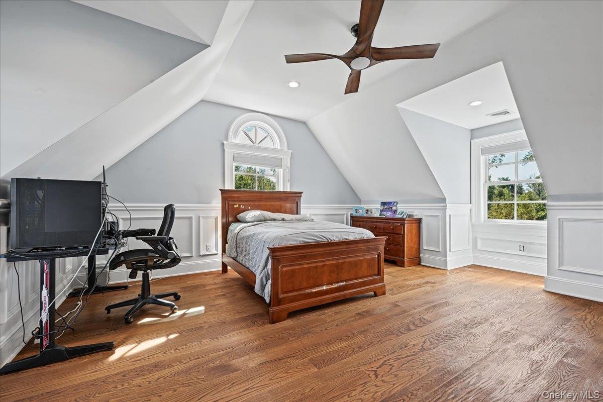 Hardwood flooring, two windows with white trim, recessed lighting, ceiling fan, and wainscoting details