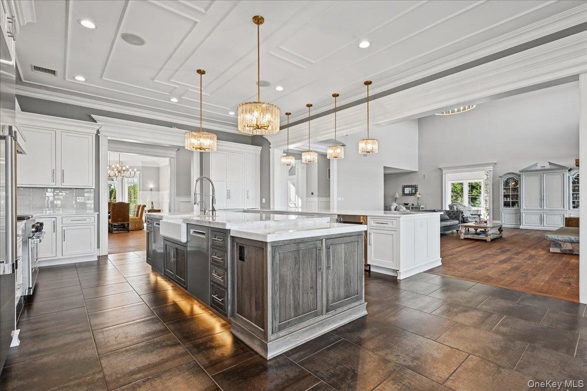 Gourmet kitchen featuring a large central island with farmhouse sink, decorative pendant lighting, white shaker cabinetry, and stone tile flooring