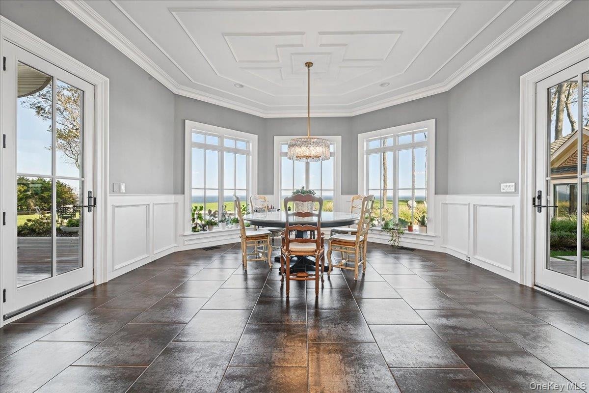 Coffered ceiling with a chandelier, wainscoting, multiple large windows, and dark tile flooring
