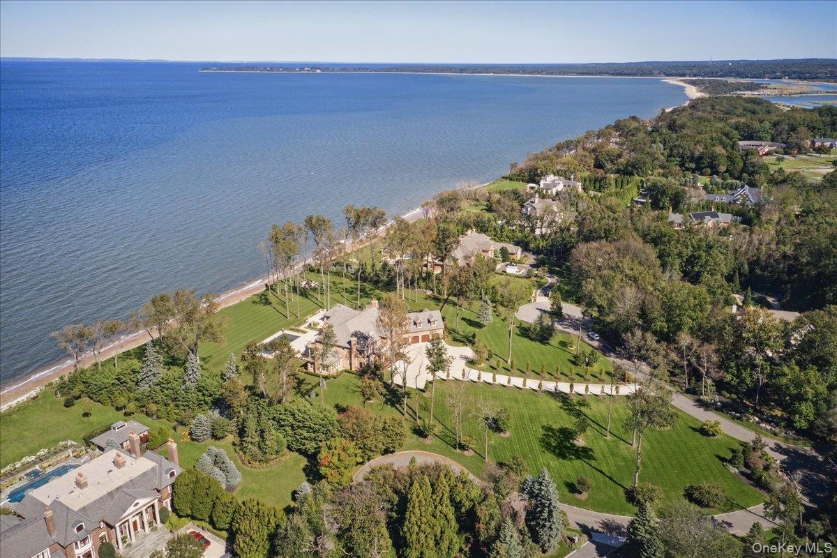 Expansive waterfront property featuring a large residence with a multi-gabled roofline, extensive manicured lawns, mature trees, and a swimming pool