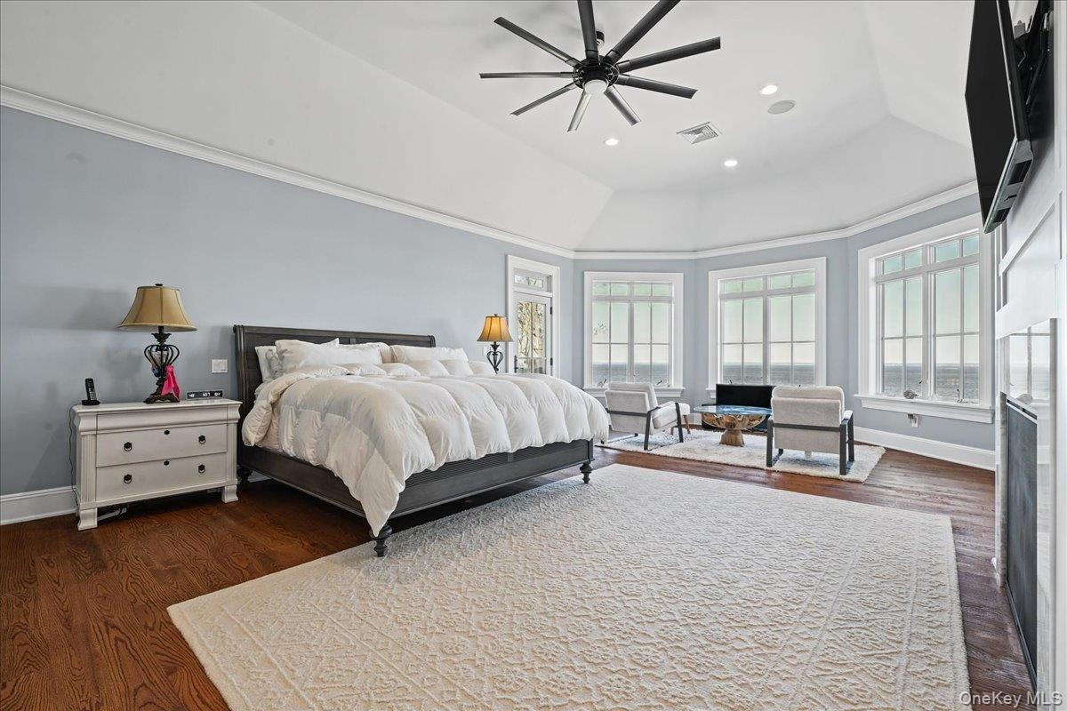 Vaulted ceiling with a contemporary ceiling fan, multiple large windows, wood-finish flooring, and crown molding
