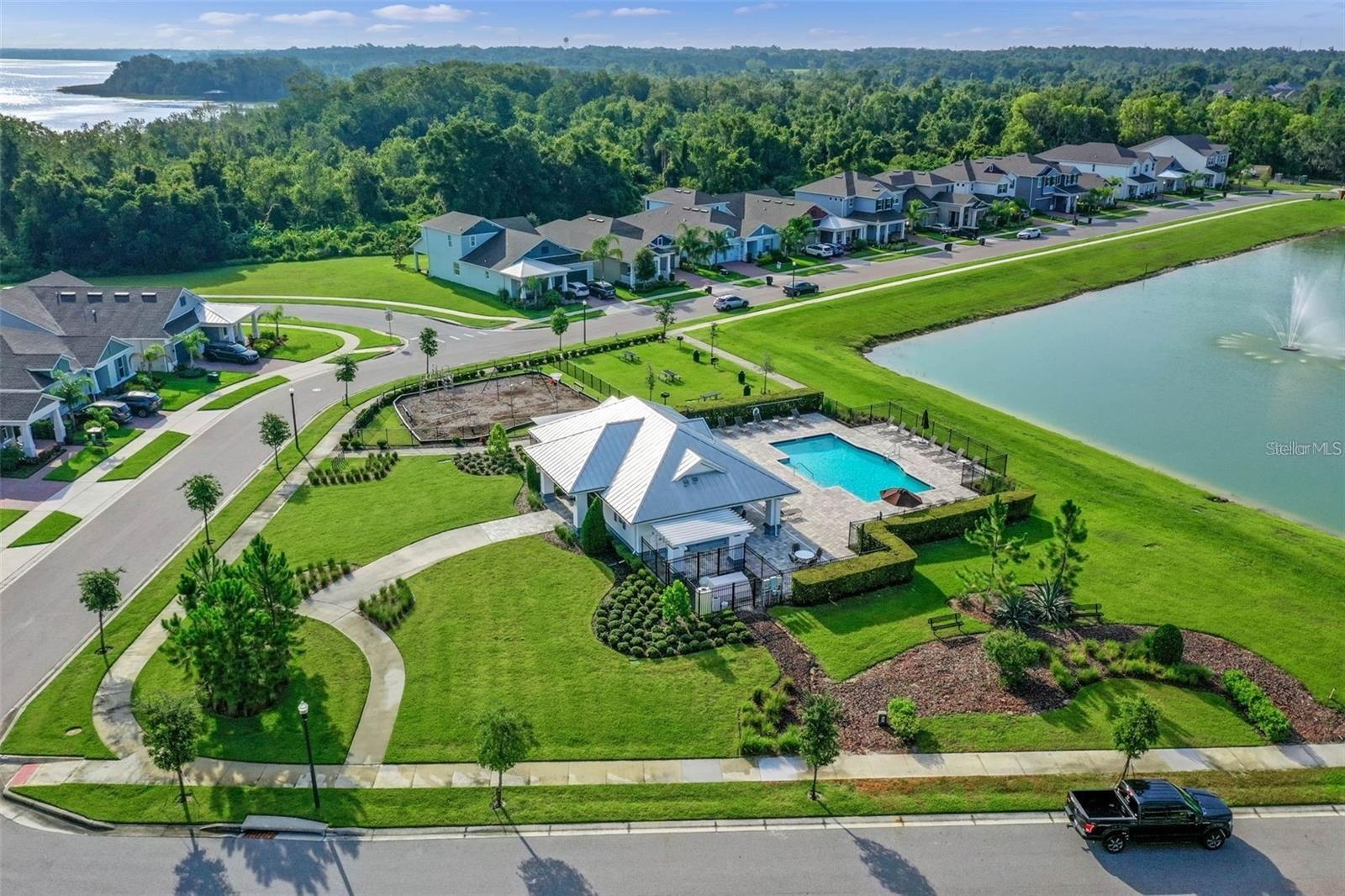 Aerial view of the community pool, playground, and landscaped walking paths beside a scenic pond.