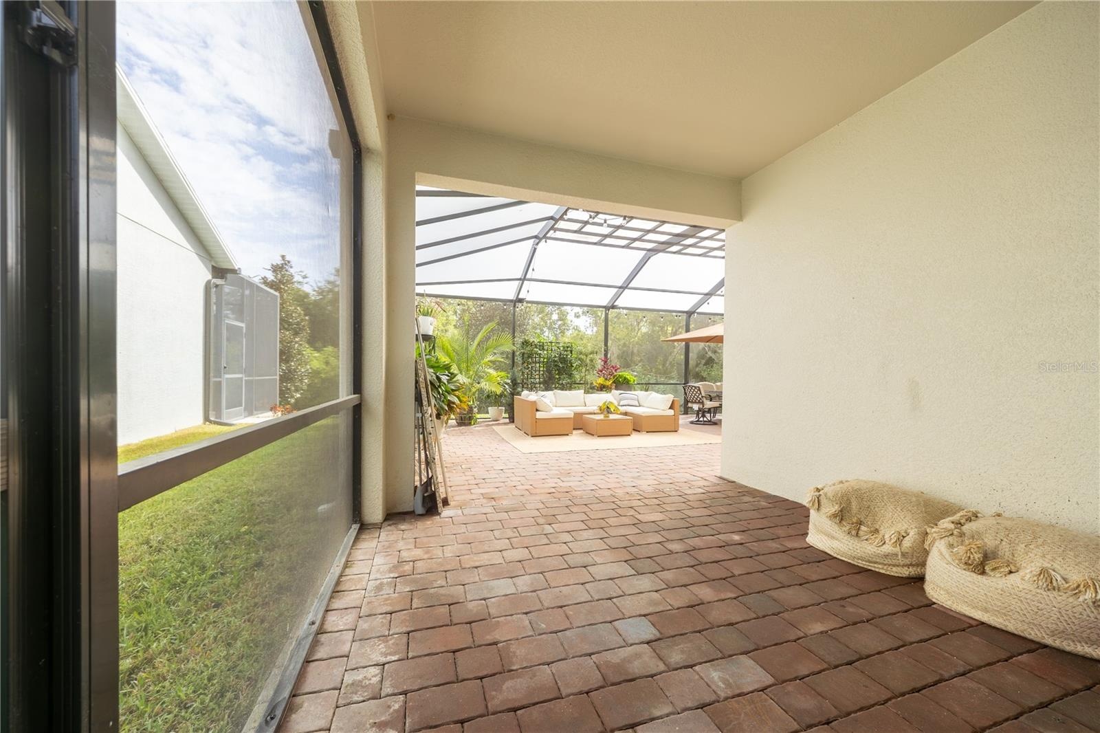 Covered lanai with paver flooring opening to an expansive screened patio with lounge and dining areas.