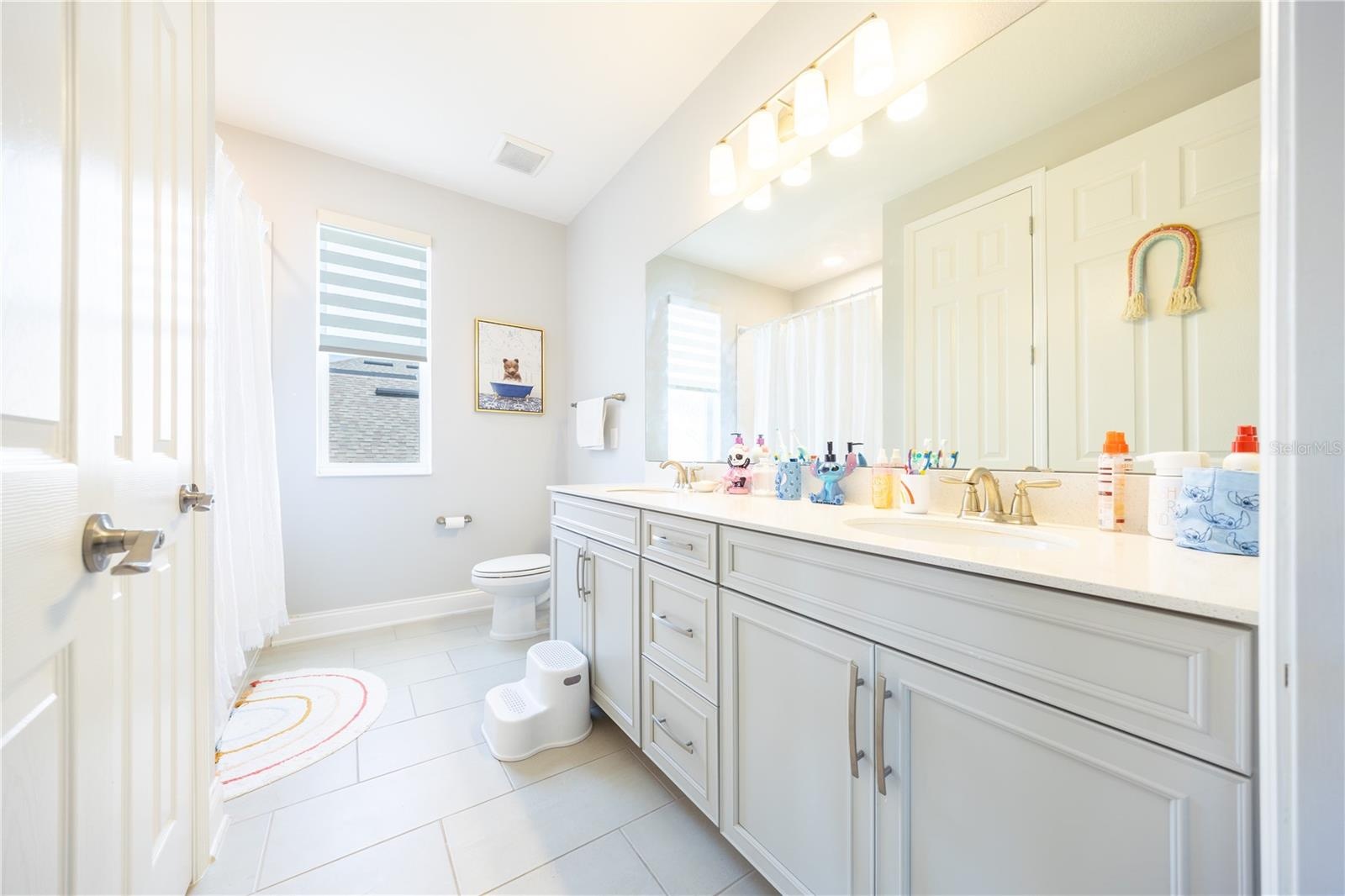 Spacious bathroom with a dual-sink vanity, expansive mirror, and ample cabinet storage.