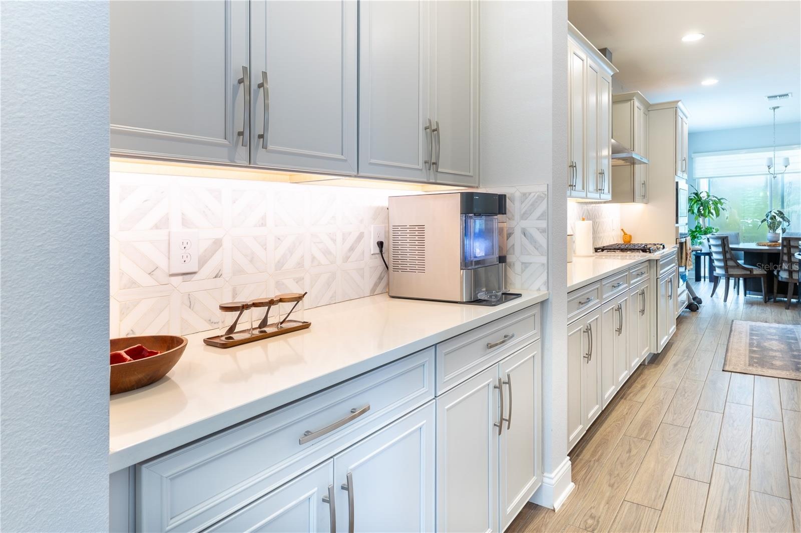 Stylish serving area with white cabinetry, geometric tile backsplash, and under-cabinet lighting.