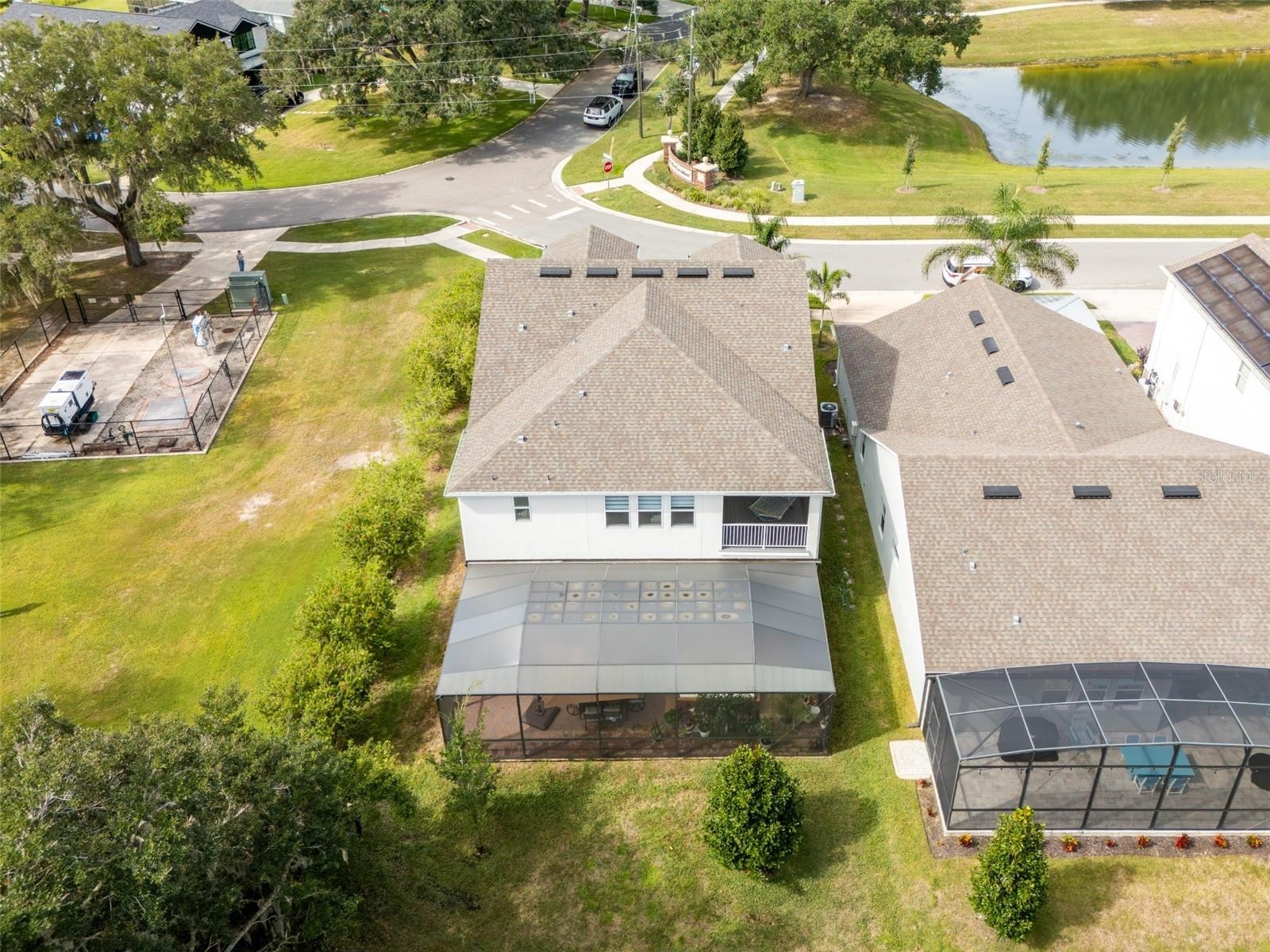 Rear aerial view showcasing an expansive screened patio, covered upstairs balcony, and wooded surroundings.