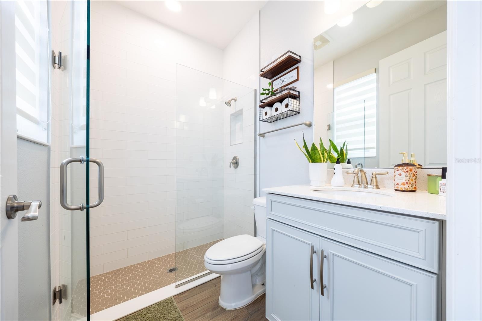 Bright bathroom with a frameless glass shower, white tile, mosaic shower floor, and light blue vanity.