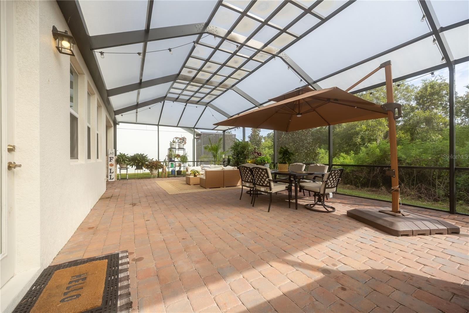 Expansive screened patio with paver flooring, outdoor dining, and peaceful conservation views.