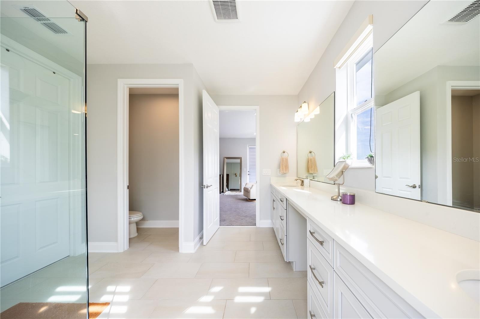 Elegant primary bathroom with an expansive vanity, makeup area, and separate toilet room.