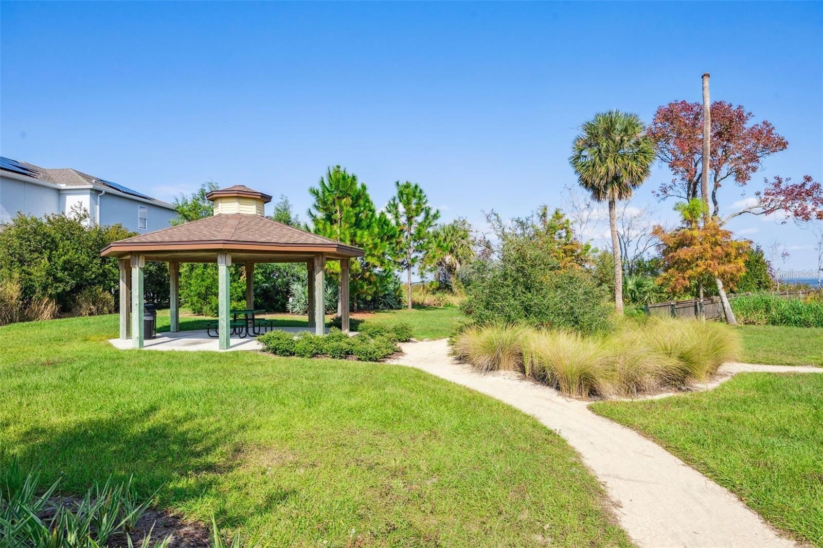 Covered picnic pavilion surrounded by lush landscaping, with a walking path leading toward the lake.