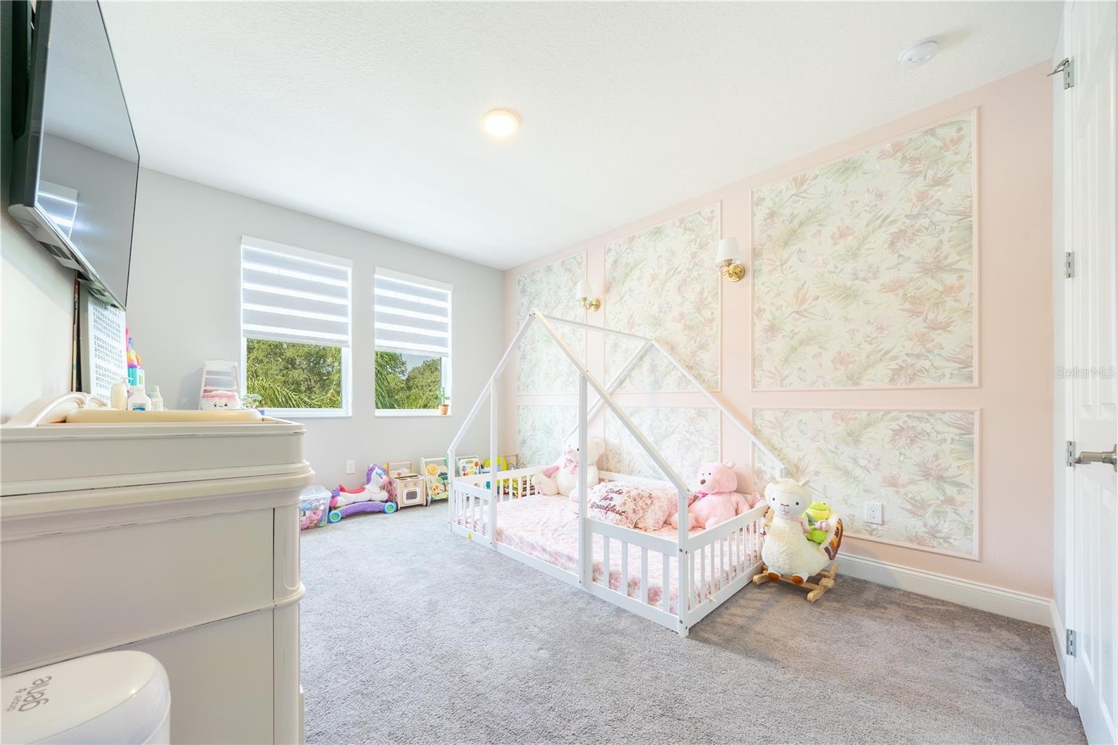 Charming bedroom with a floral accent wall, decorative sconces, and windows with lake views.