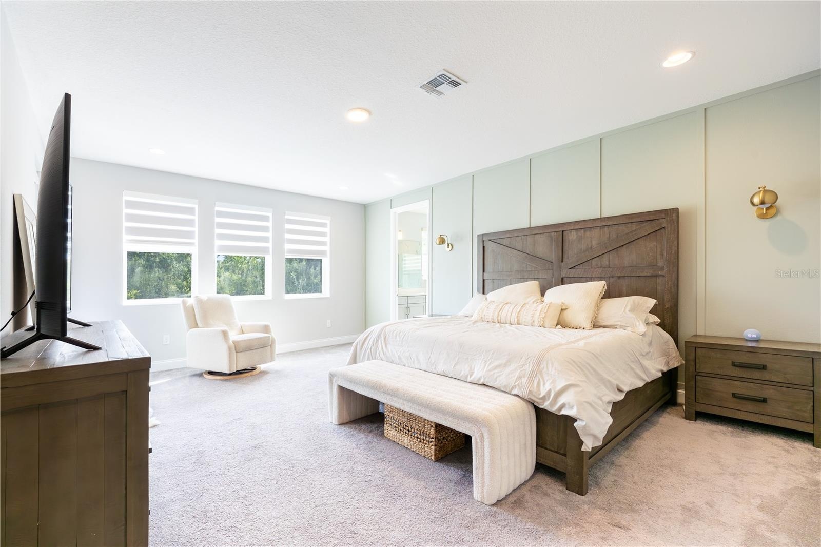 Spacious primary bedroom with an elegant accent wall, sitting area, and porch access with views of a conservation area.