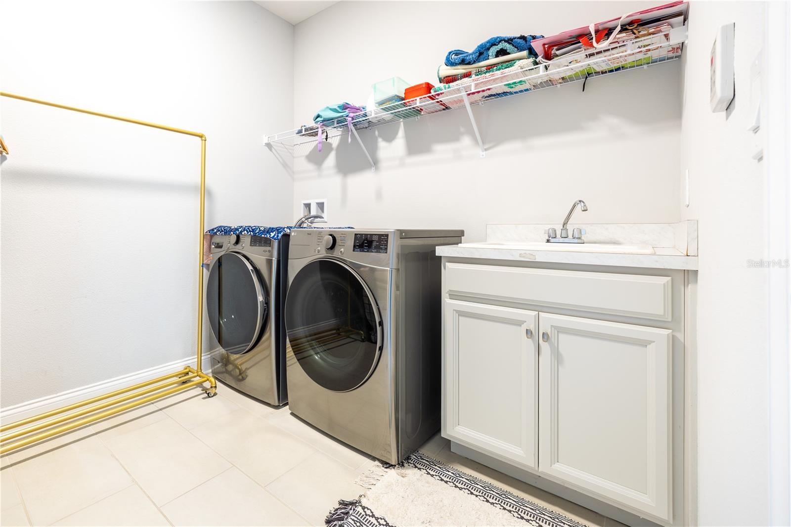 Laundry room with included front-load washer and dryer, utility sink, and storage shelving.