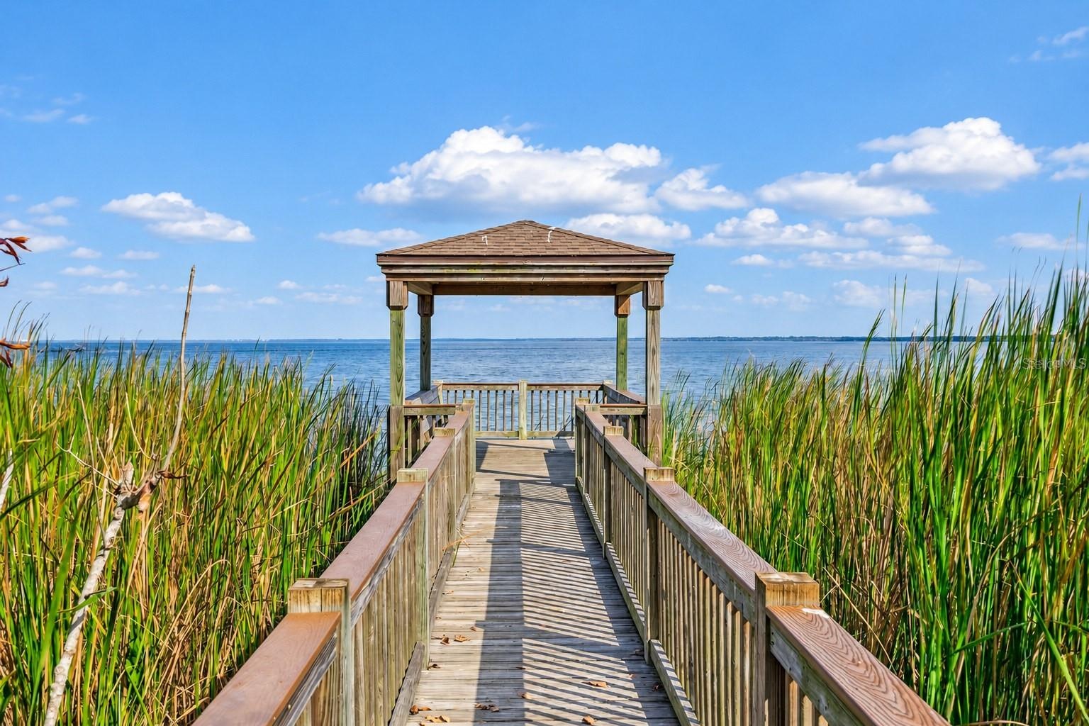 Community boardwalk leading to a covered lakeside gazebo with sweeping water views.