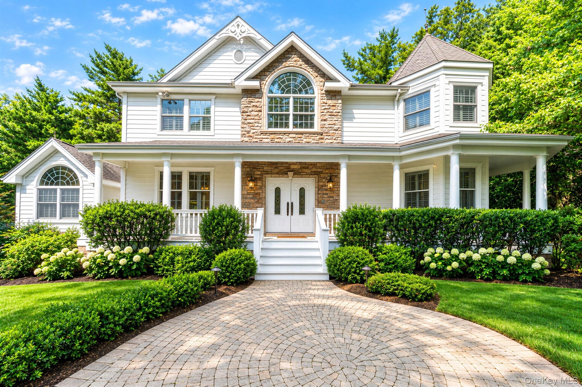 Classic Colonial-style residence featuring a brick and stone facade with white siding, arched entryway with decorative transom window, and a covered f