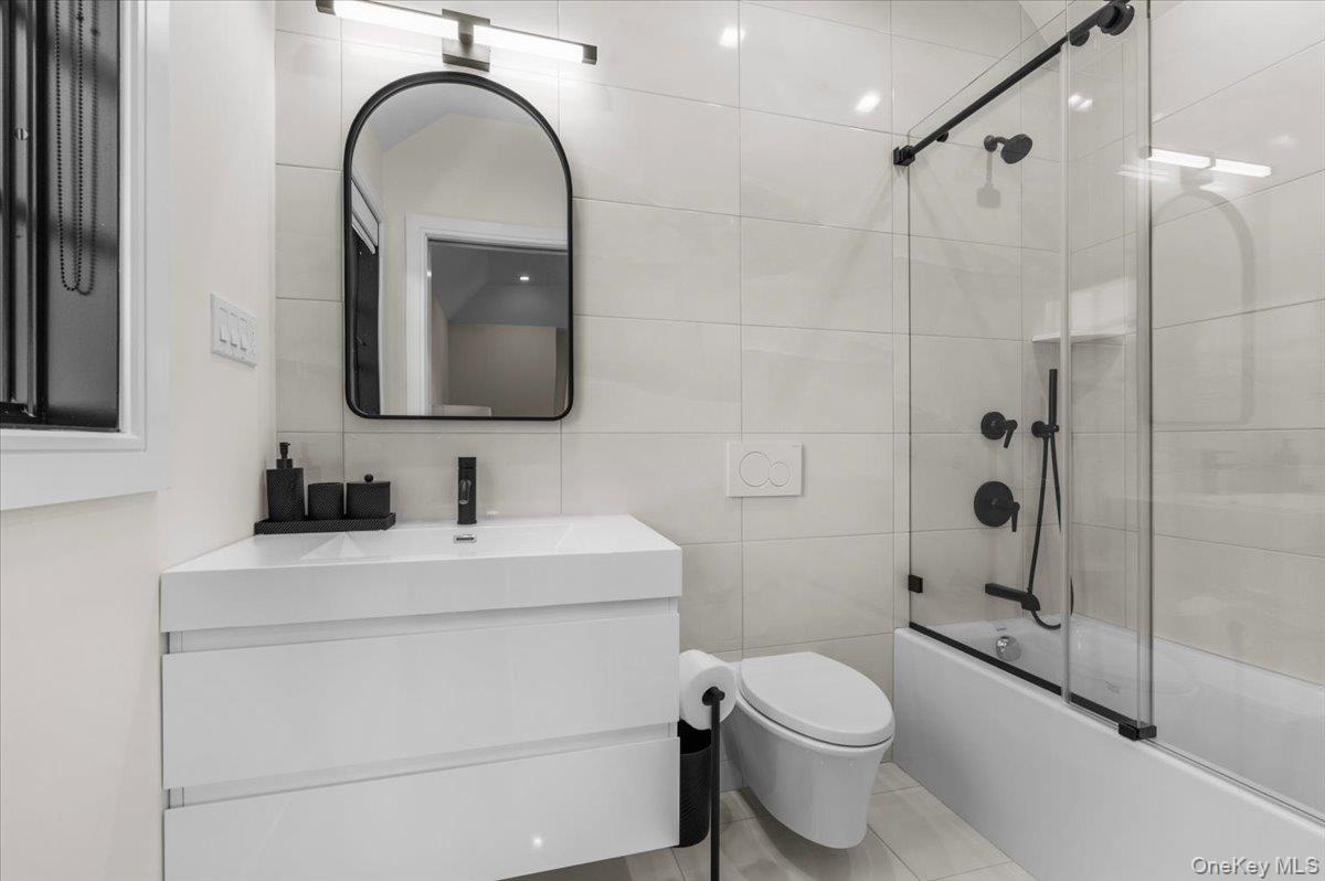 Floating vanity with integrated sink, black-framed arched mirror, black matte fixtures, and full-height wall tiling
