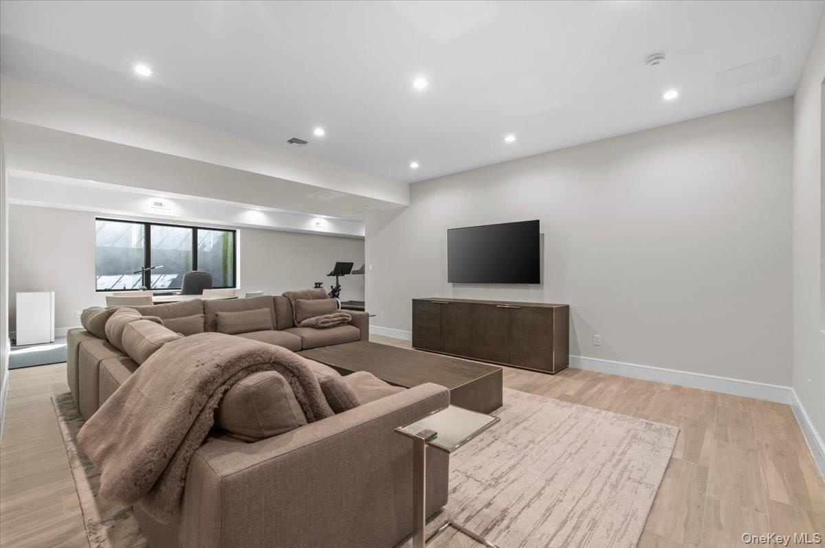 Recessed lighting, light wood-finish flooring, built-in media console, large windows, and a dedicated fitness area