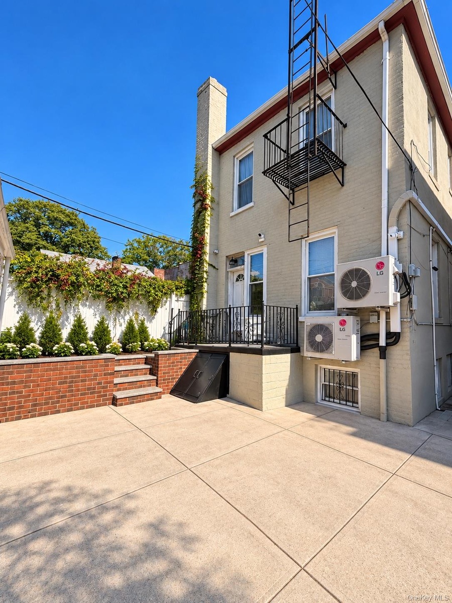 Paved exterior patio with a brick-faced raised planter, built-in steps, and a wrought iron balcony