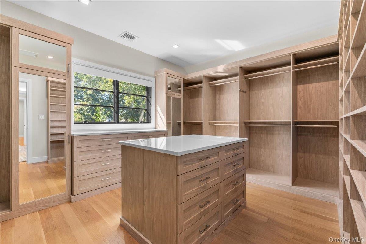 Custom wood-finish cabinetry, built-in shelving, integrated drawers, central island with countertop, and wood-finish flooring