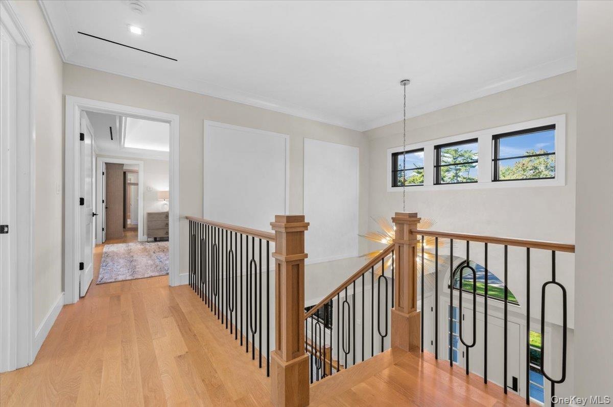 Hardwood flooring, wood newel post, black wrought iron balusters, recessed lighting, and white trim molding