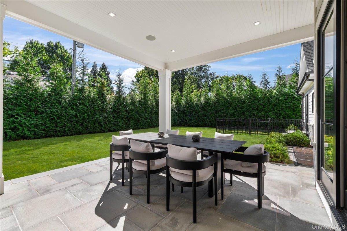 Covered outdoor patio with recessed lighting, large format pavers, and a manicured lawn