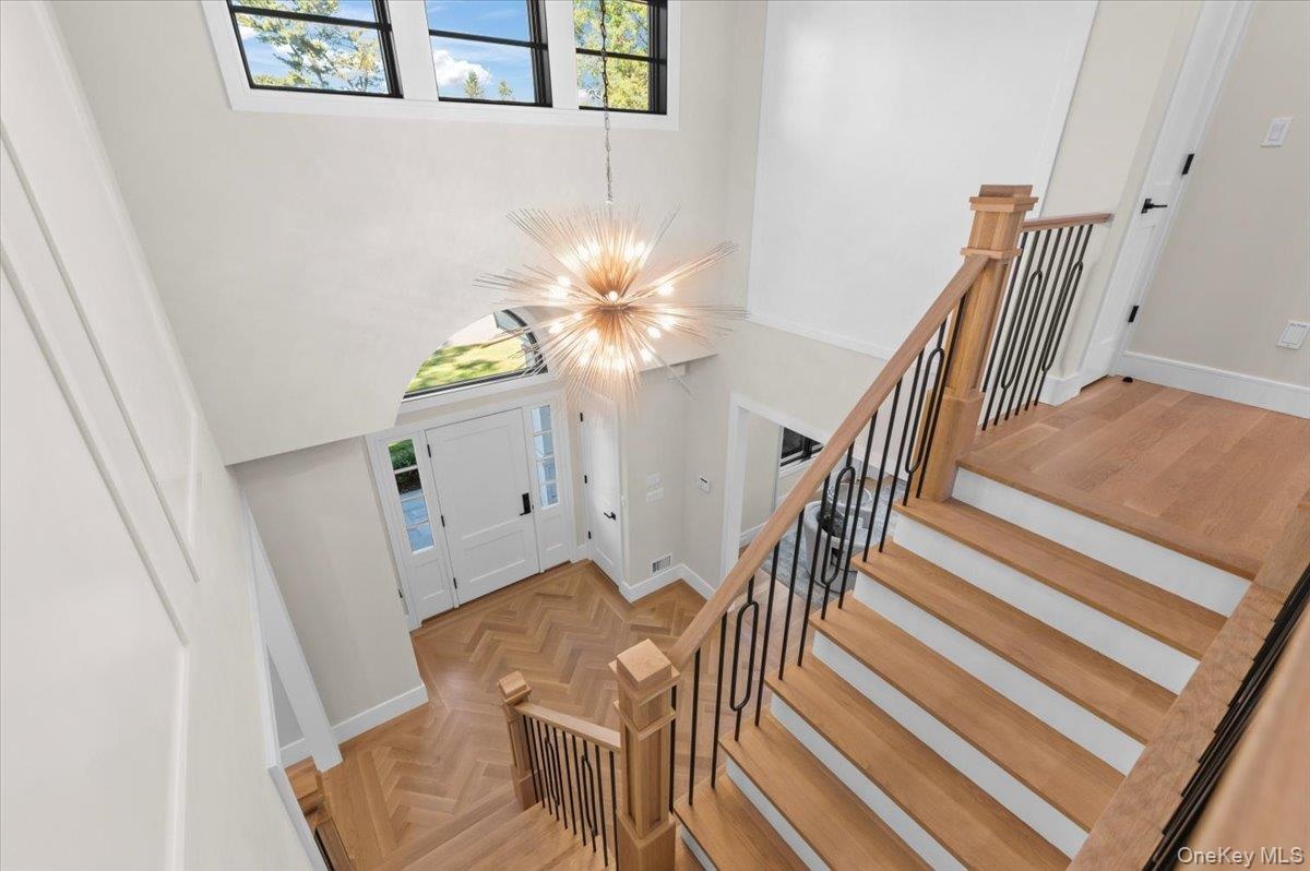 Two-story entry foyer featuring a striking chandelier, herringbone wood-finish flooring, and a grand staircase with wrought iron balusters