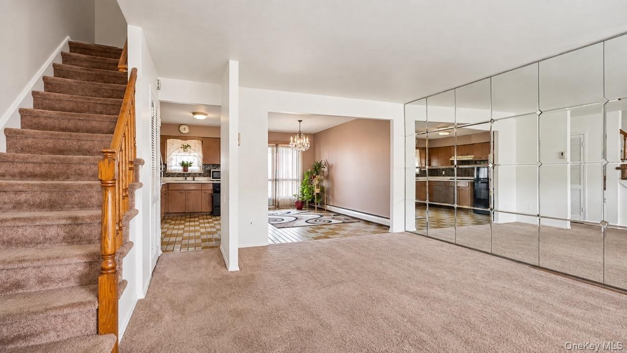 Carpeted staircase with wood railing, wall-mounted mirrored panels, and visible kitchen with wood-finish cabinetry