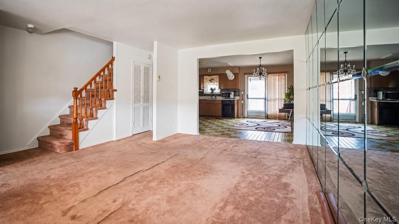 Staircase with wood railing and carpeted treads, mirrored wall, wood finish cabinetry, and chandelier