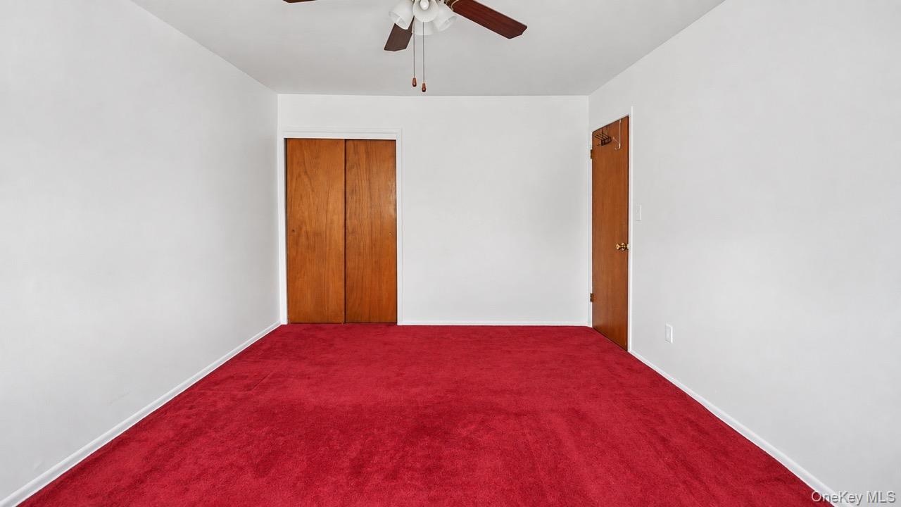 Room featuring red carpeting, white painted walls, a ceiling fan, and wood-finish doors