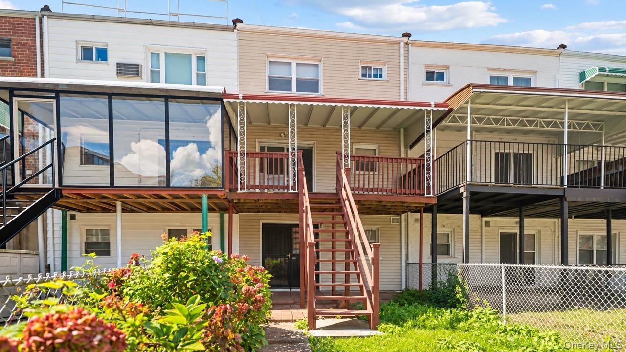 Rear exterior featuring a glass-enclosed sunroom, upper-level deck with awning, wood stairs, and chain-link fencing