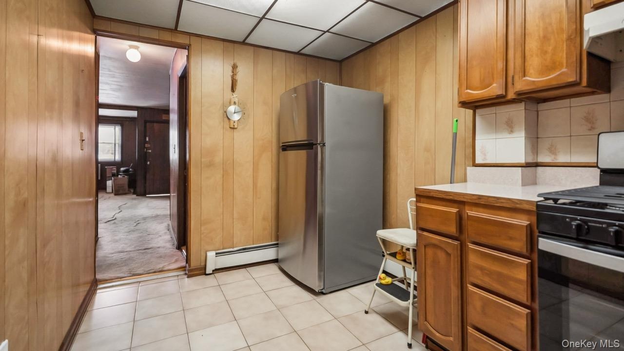 Kitchen with stainless steel refrigerator, tile flooring, wood-finish cabinetry, and a gas range