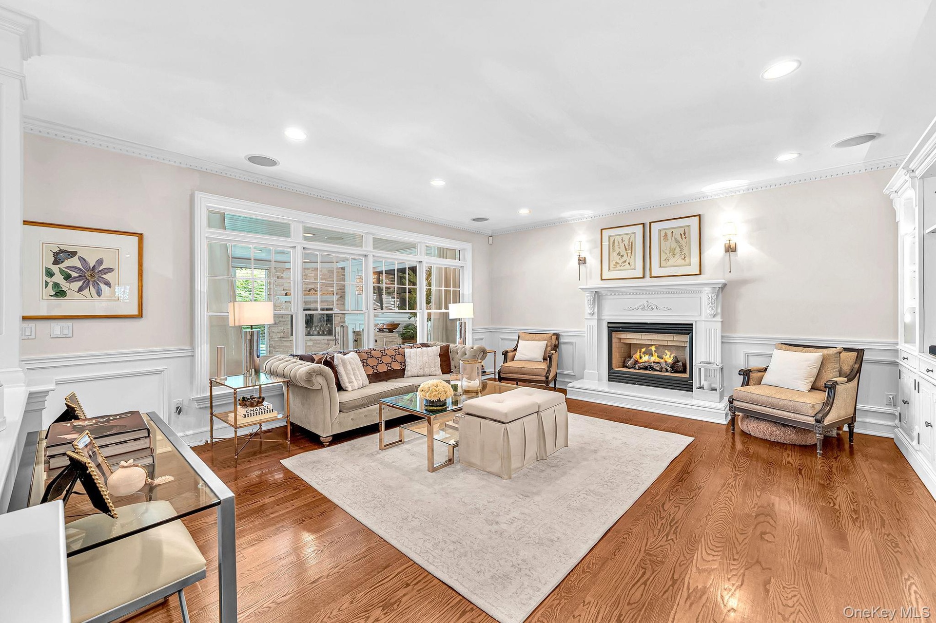 Elegant living room featuring hardwood flooring, a gas fireplace with decorative surround and mantel, recessed ceiling lighting, large multi-pane wind