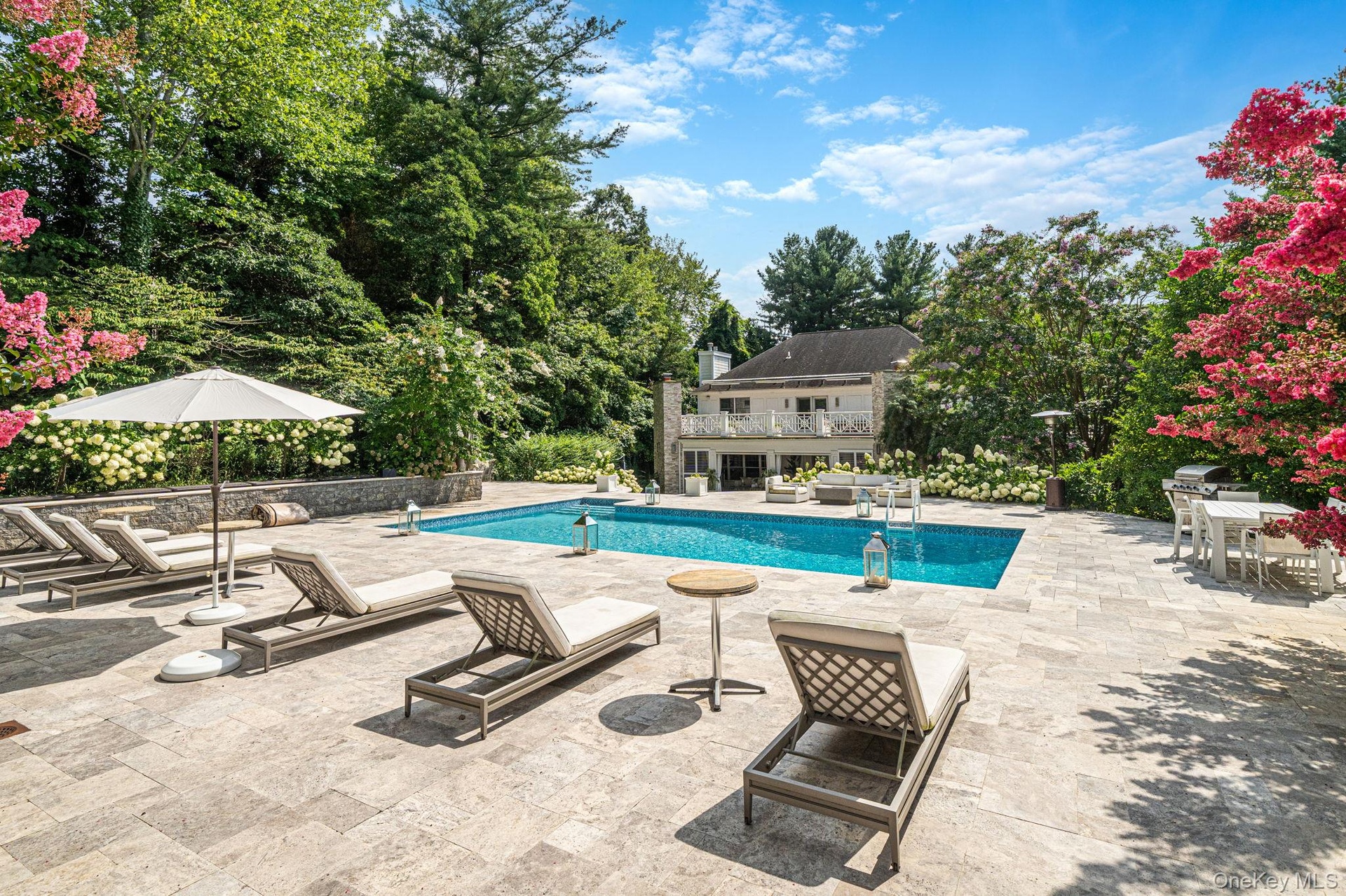 Expansive hardscape patio featuring a resort-style saltwater swimming pool with integrated spa, multiple lounge chairs, and market umbrellas