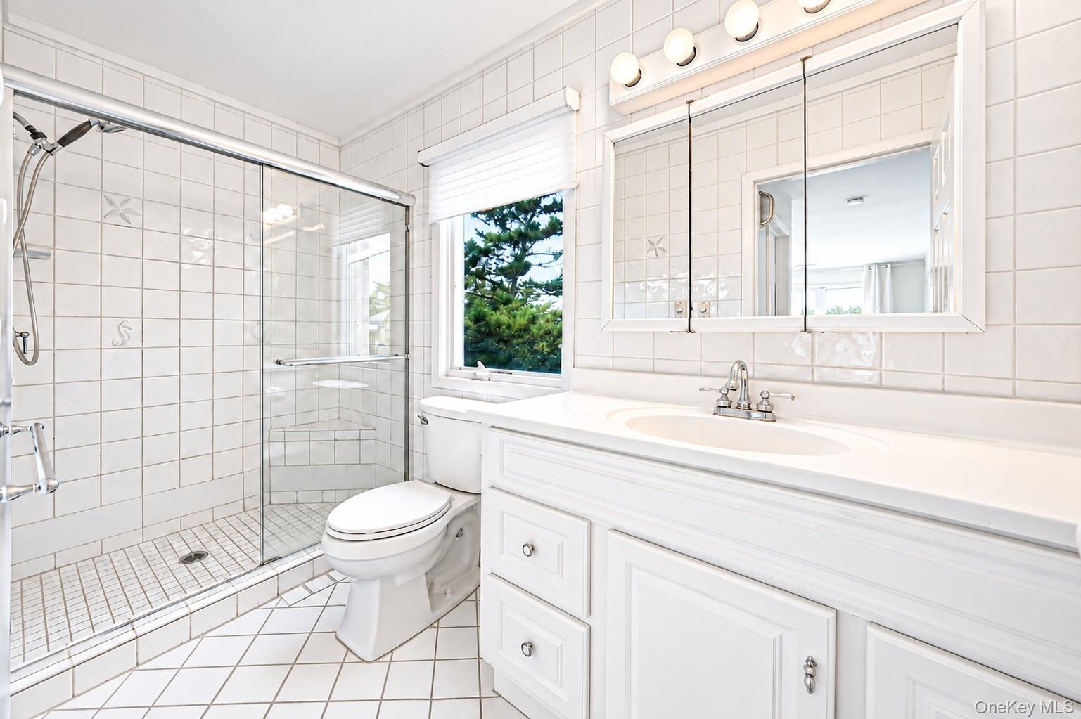 White tiled bathroom featuring a glass-enclosed shower, single vanity