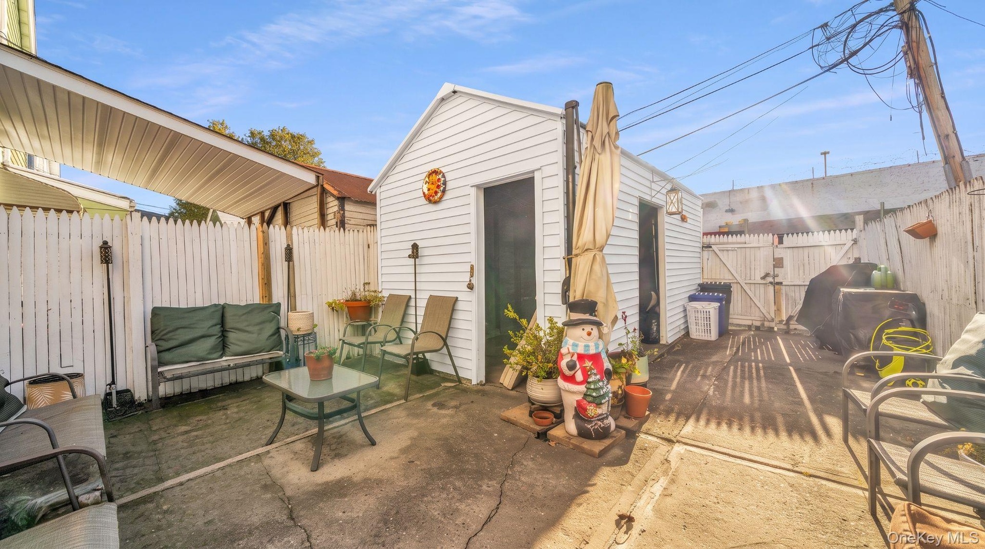 Expansive concrete patio area with a white picket fence, covered patio section, and a standalone storage structure