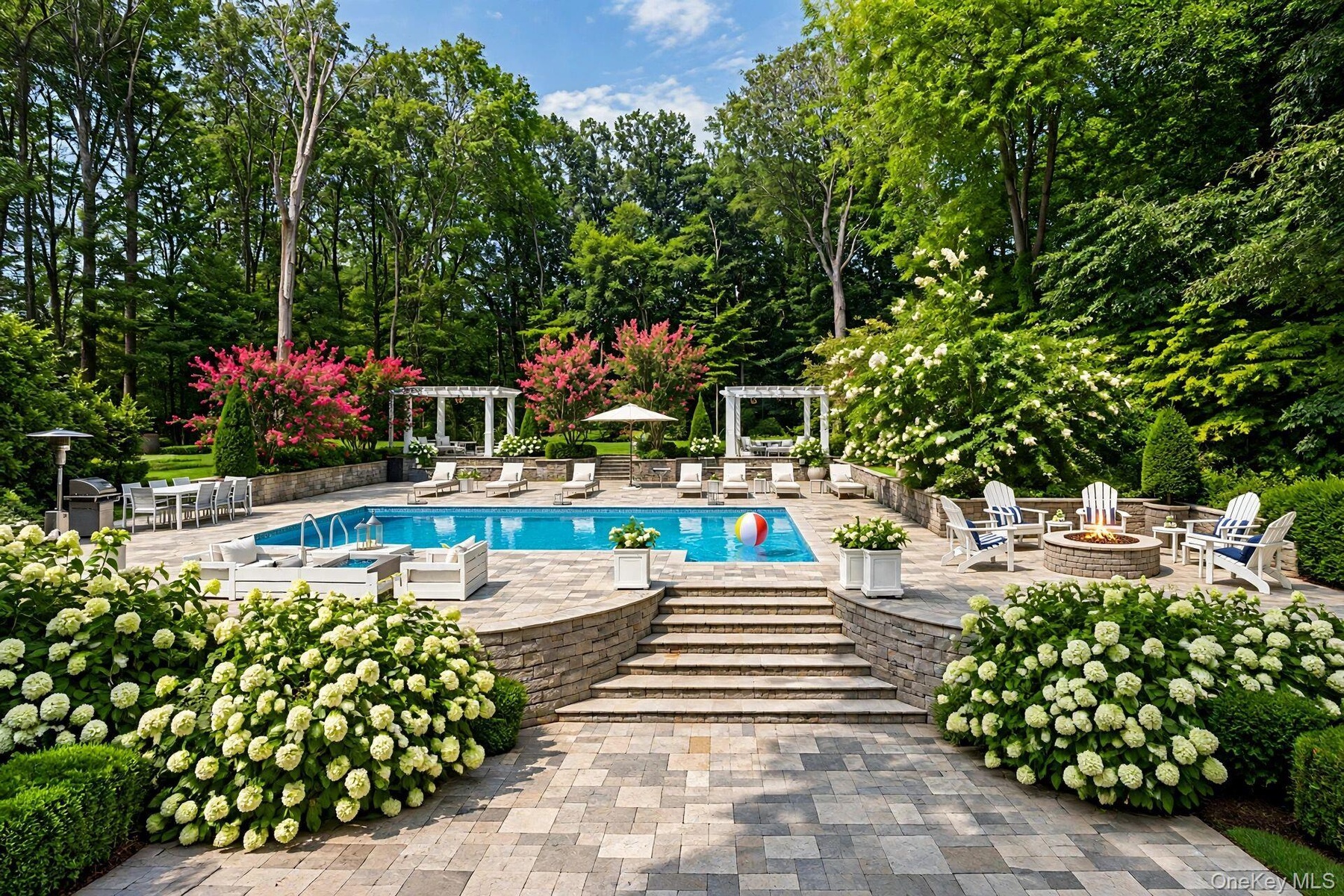 Expansive outdoor living area featuring a swimming pool, stone paver patio, integrated fire pit, and tiered landscaping