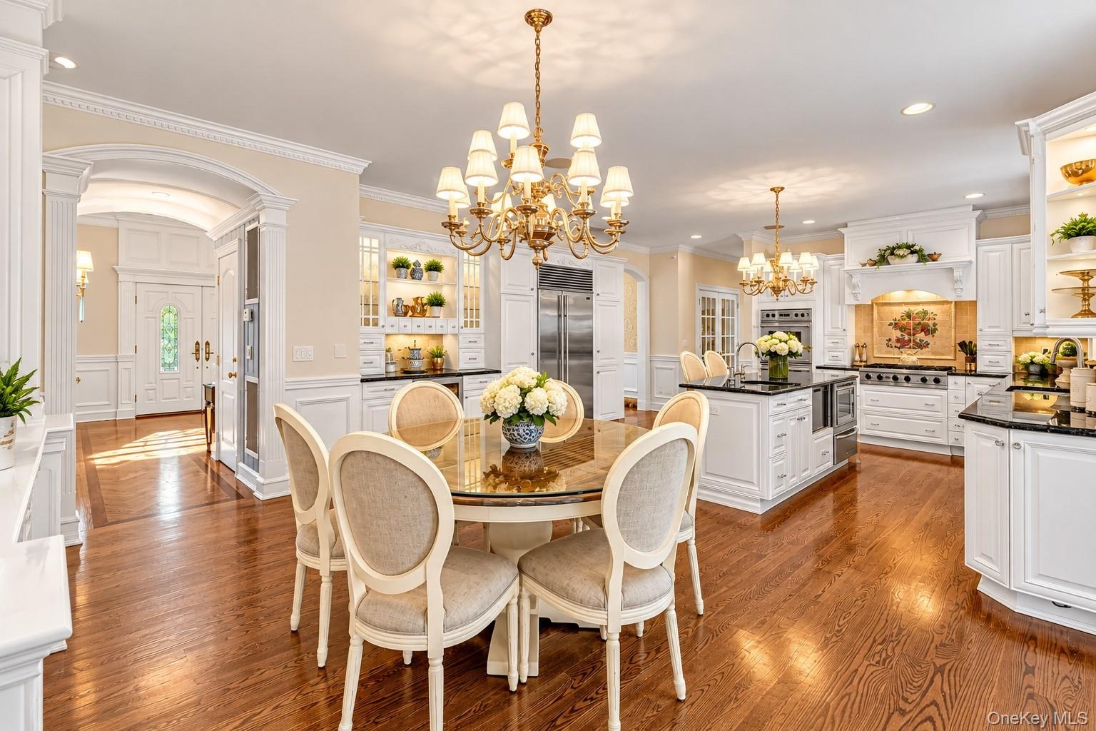 Spacious open-concept kitchen with wood-finish flooring, white cabinetry, dark countertops, and a central island with a sink