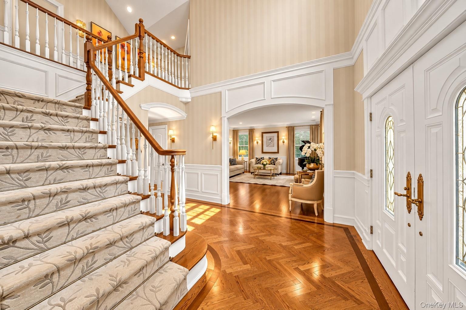 Grand foyer featuring a dual-level staircase with white balusters and wood handrails, herringbone wood flooring, decorative wall molding, and arched d