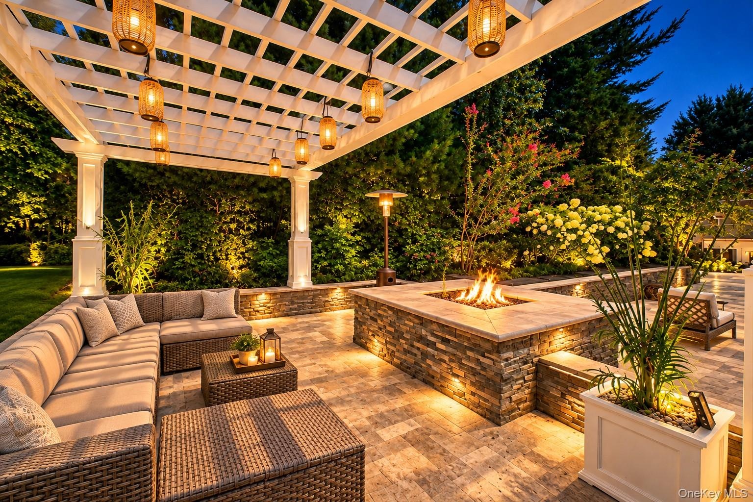 Expansive patio featuring a white pergola with hanging lanterns, a built-in stone fire pit, integrated lighting, and paver flooring