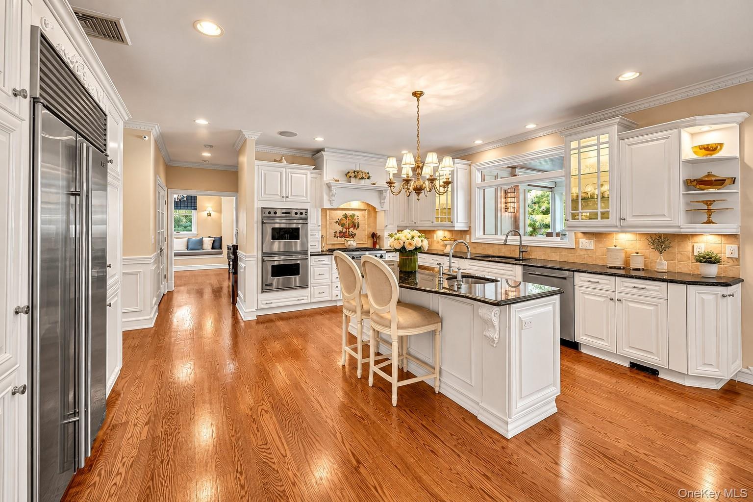 Hardwood flooring, stainless steel appliances, white cabinetry with crown molding, a kitchen island with seating, and recessed lighting