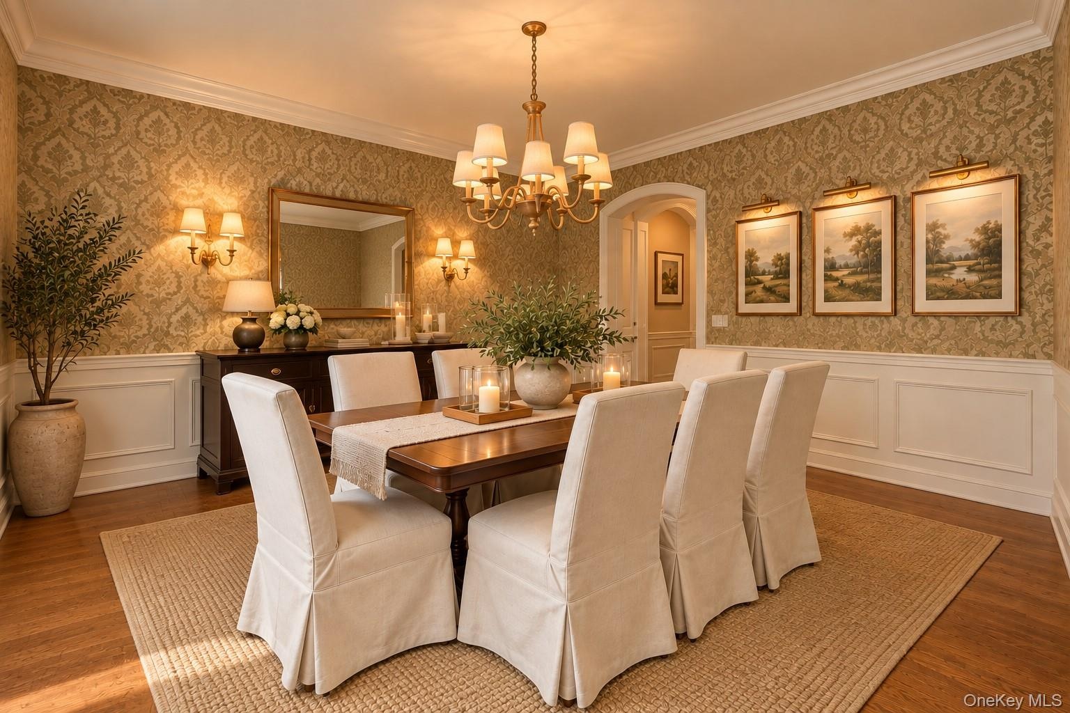 Elegant formal dining room showcasing damask-patterned wallcovering, wainscoting with crown molding, hardwood flooring, and a multi-arm brass chandeli