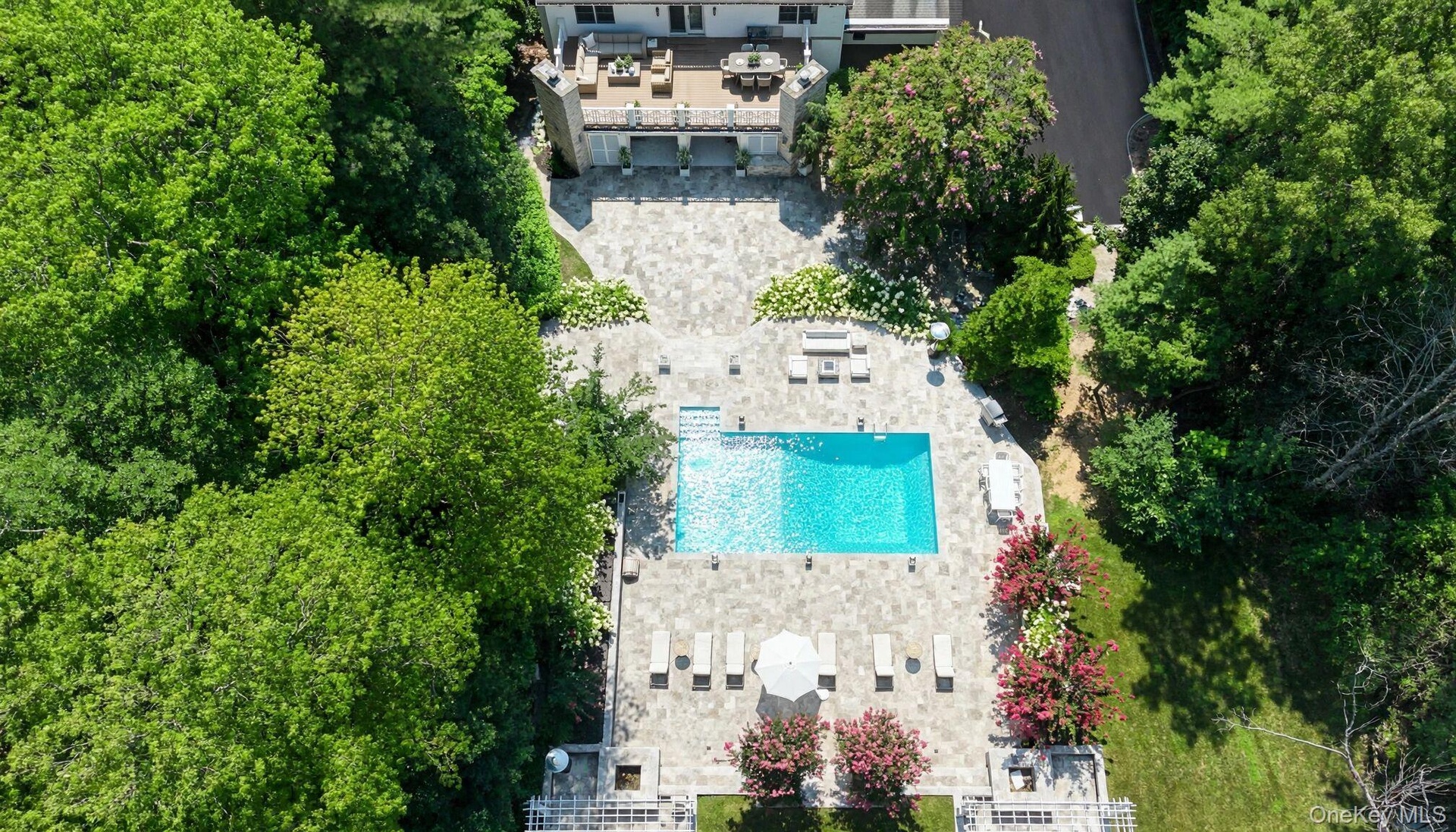 Expansive outdoor living space featuring a rectangular swimming pool, extensive paver patio, and mature landscaping